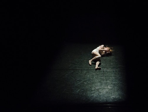 Woman lying on a blank, black floor with a spotlight on her. 